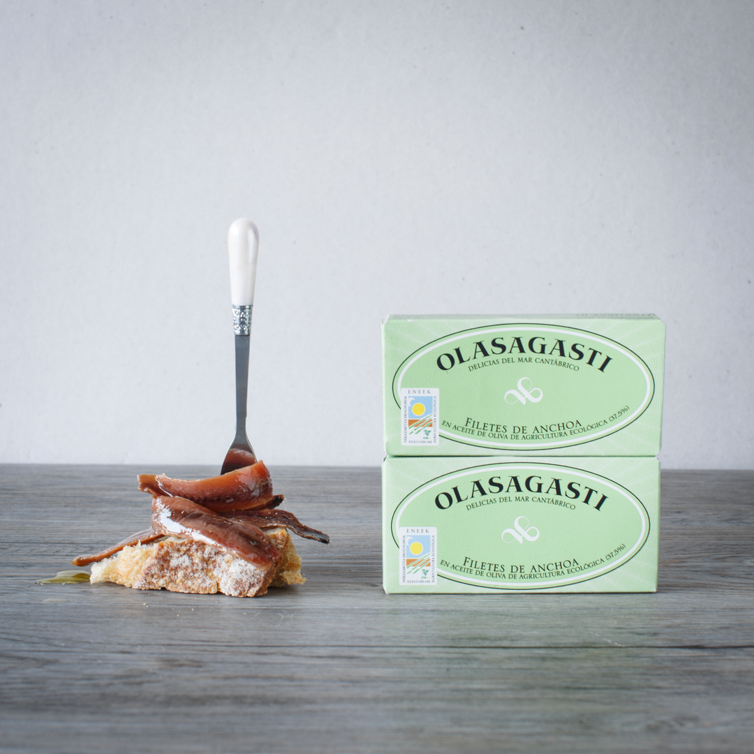 Anchovies Packaging Packaging - in Organic Olive Oil, by Olasagasti. Piece of bread with Anchovies in Organic Olive Oil on top, held by a fork.