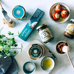Packaging of Cantabrian sea pâté, various packaging of canned preserves and glass jars, bowl with stuffed peppers, bowl with salt and bowl with olive oil.