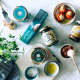 Packaging of Cantabrian sea pâté, various packaging of canned preserves and glass jars, bowl with stuffed peppers, bowl with salt and bowl with olive oil.