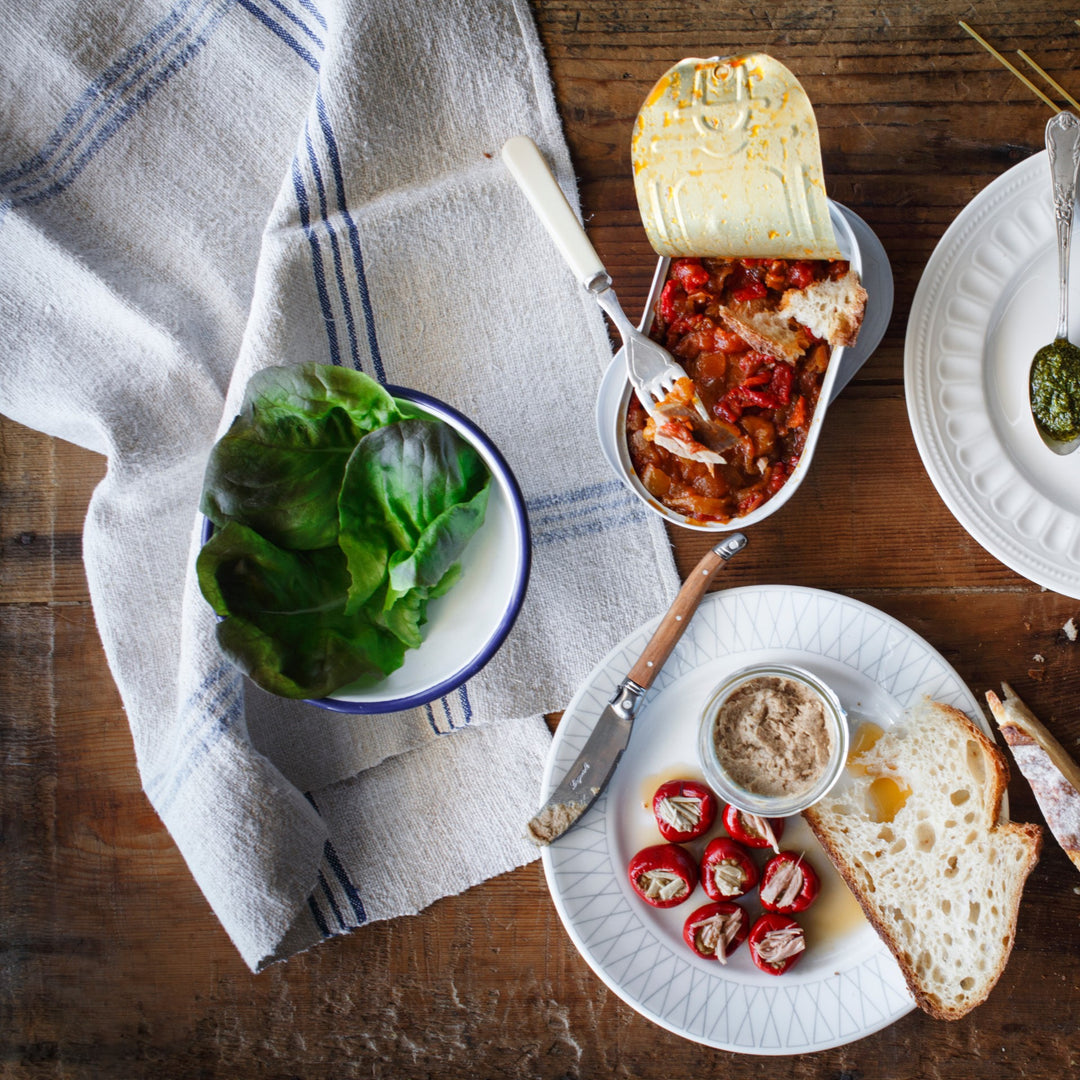 Can of tuna with peppers, plate with peppers stuffed with tuna, slice of bread, bowl with green vegetable leaves