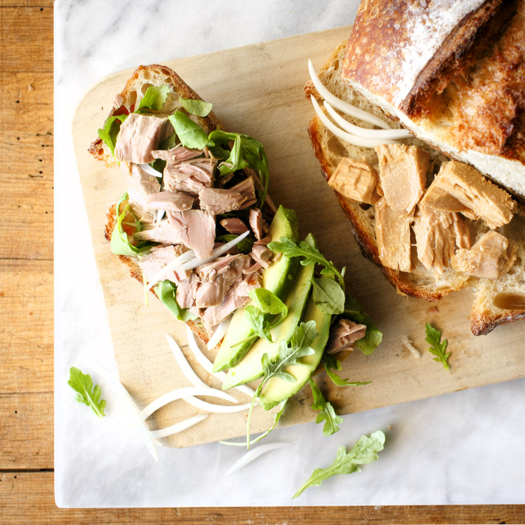 Photograph of slice of bread with tuna, onion, arugula and avocado.