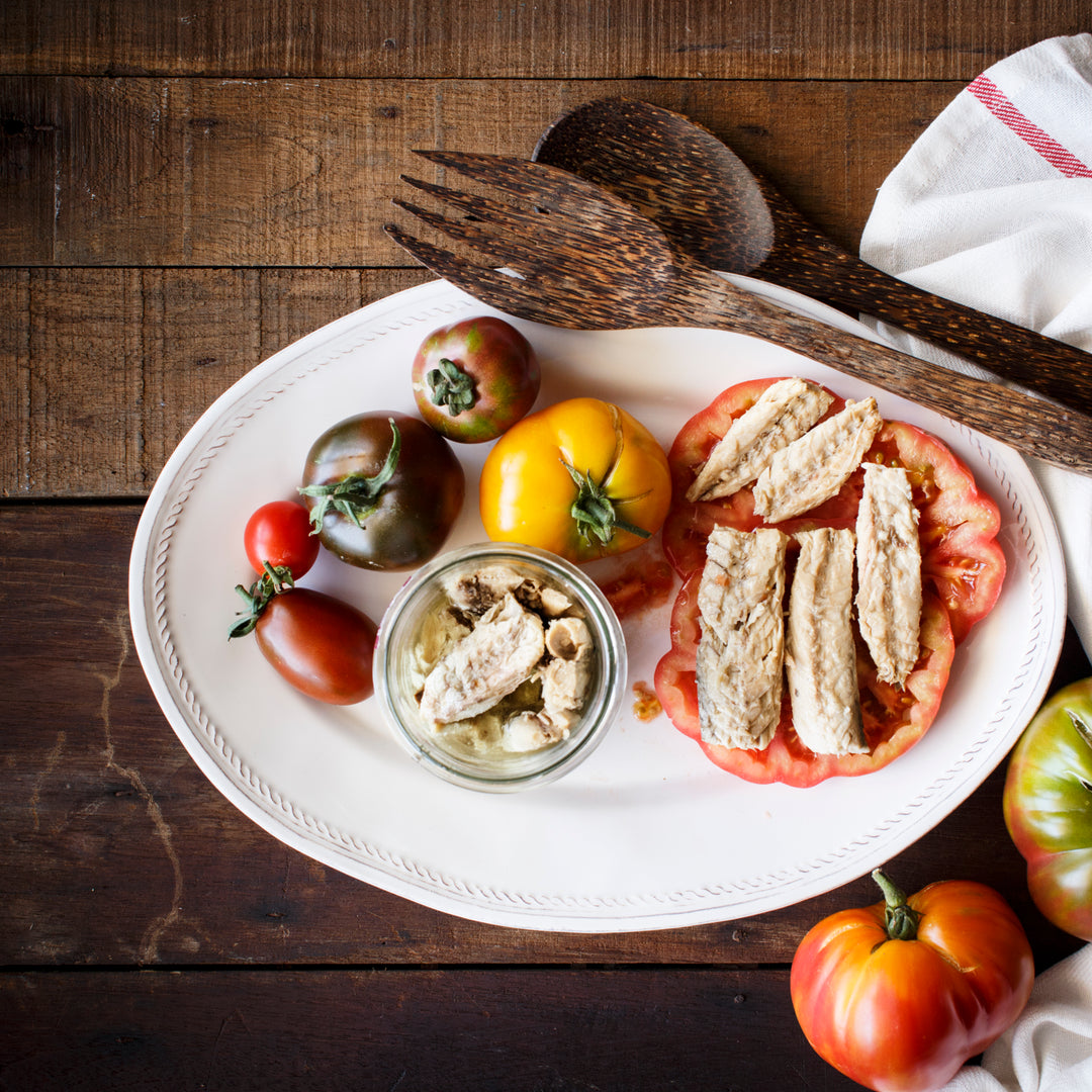 Mackerel Fillets in Organic Olive Oil on top of tomato slices, served on a platter.