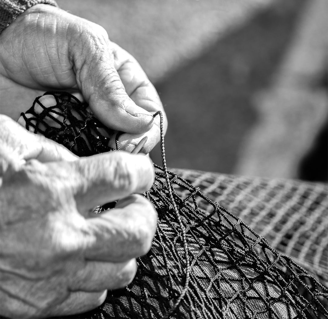 Monochrome black and white photograph of a fisherman's hands arranging a fishing net with a needle.