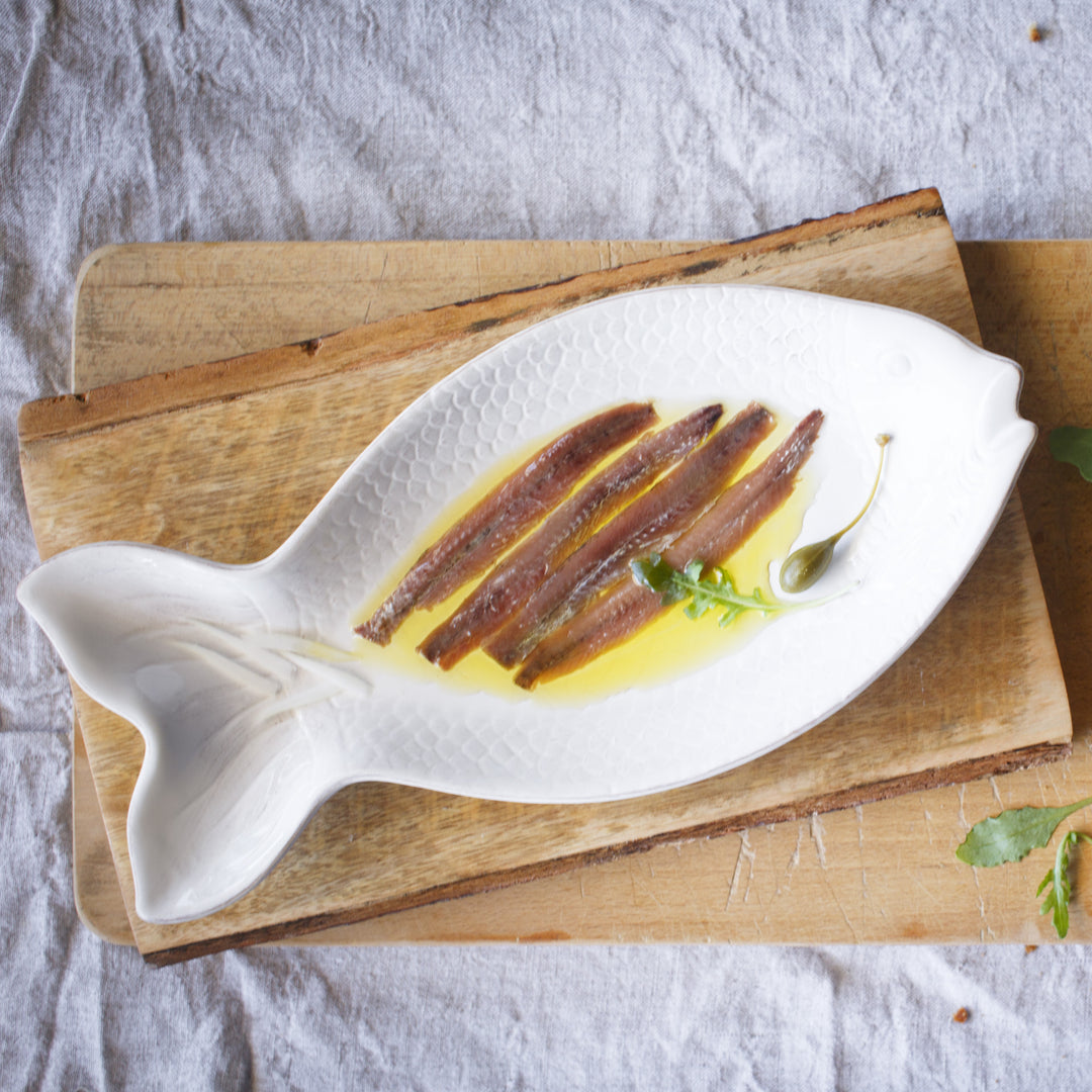Photograph of a ceramic dish in the shape of a fish, with anchovy fillets in olive oil.