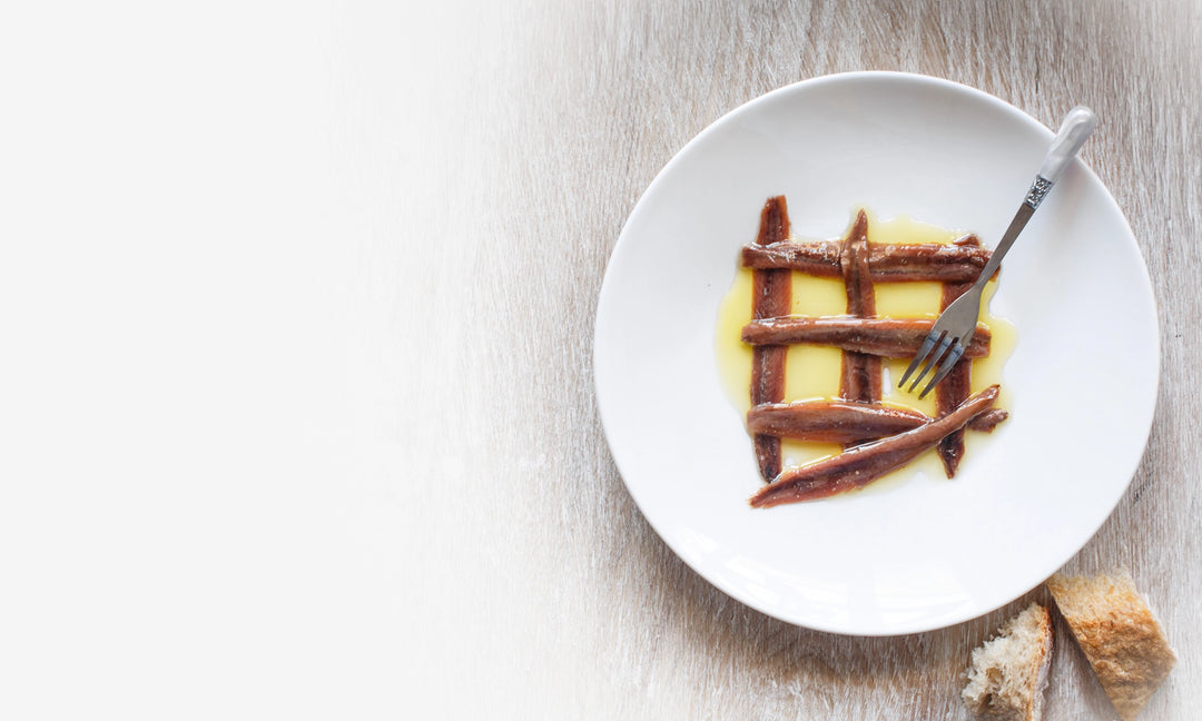 Plate with anchovy fillets in olive oil, with a fork.