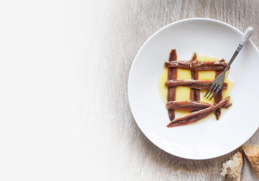 Plate with anchovy fillets in olive oil, with a fork.
