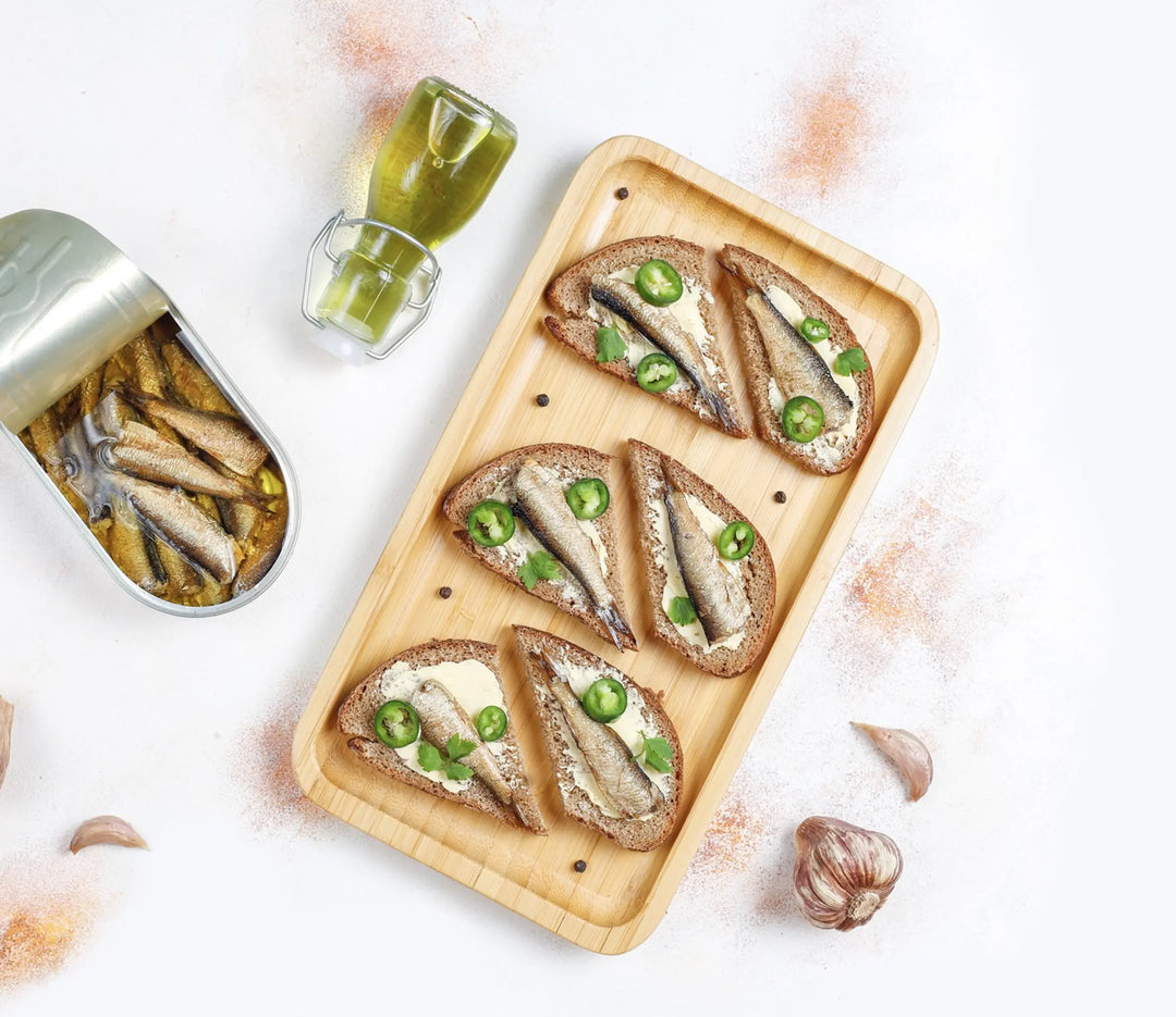 Canned sardines, sardines served on slices of bread with cream cheese and peppers, placed on a wooden board.