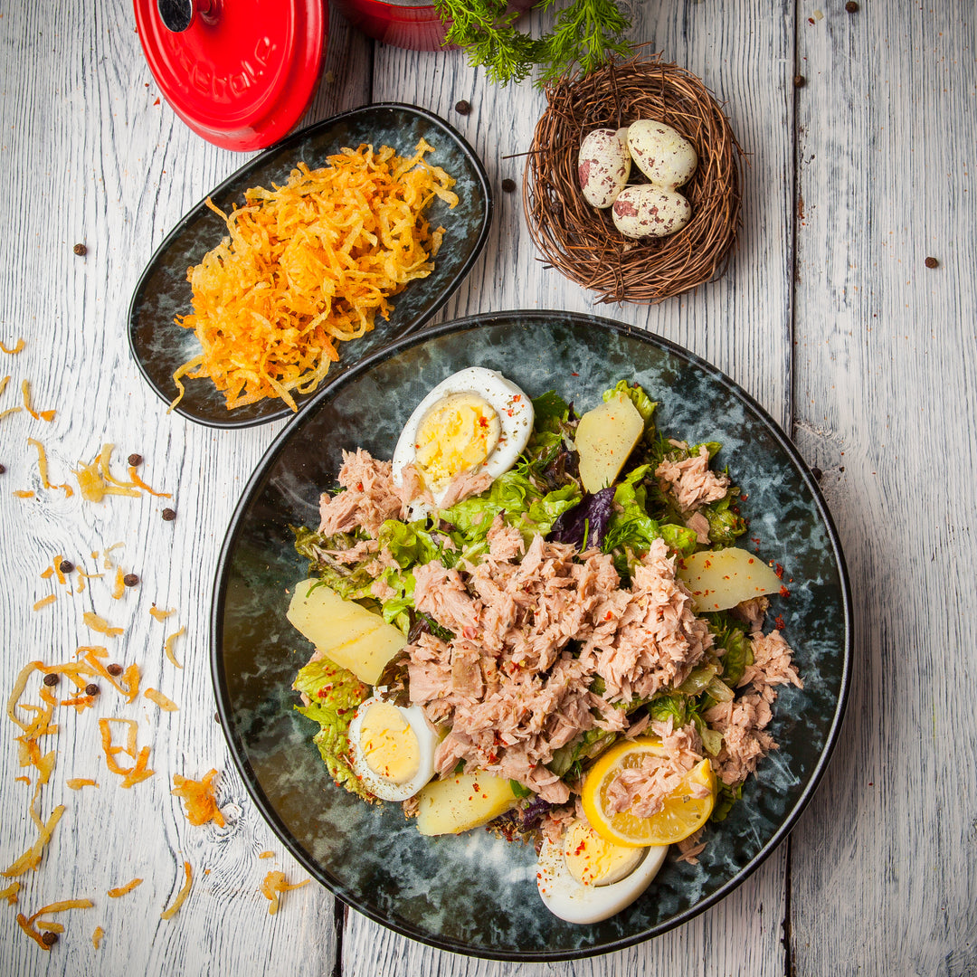 Plate with canned tuna salad with lettuce, potatoes and boiled eggs. Dish with grated carrot.